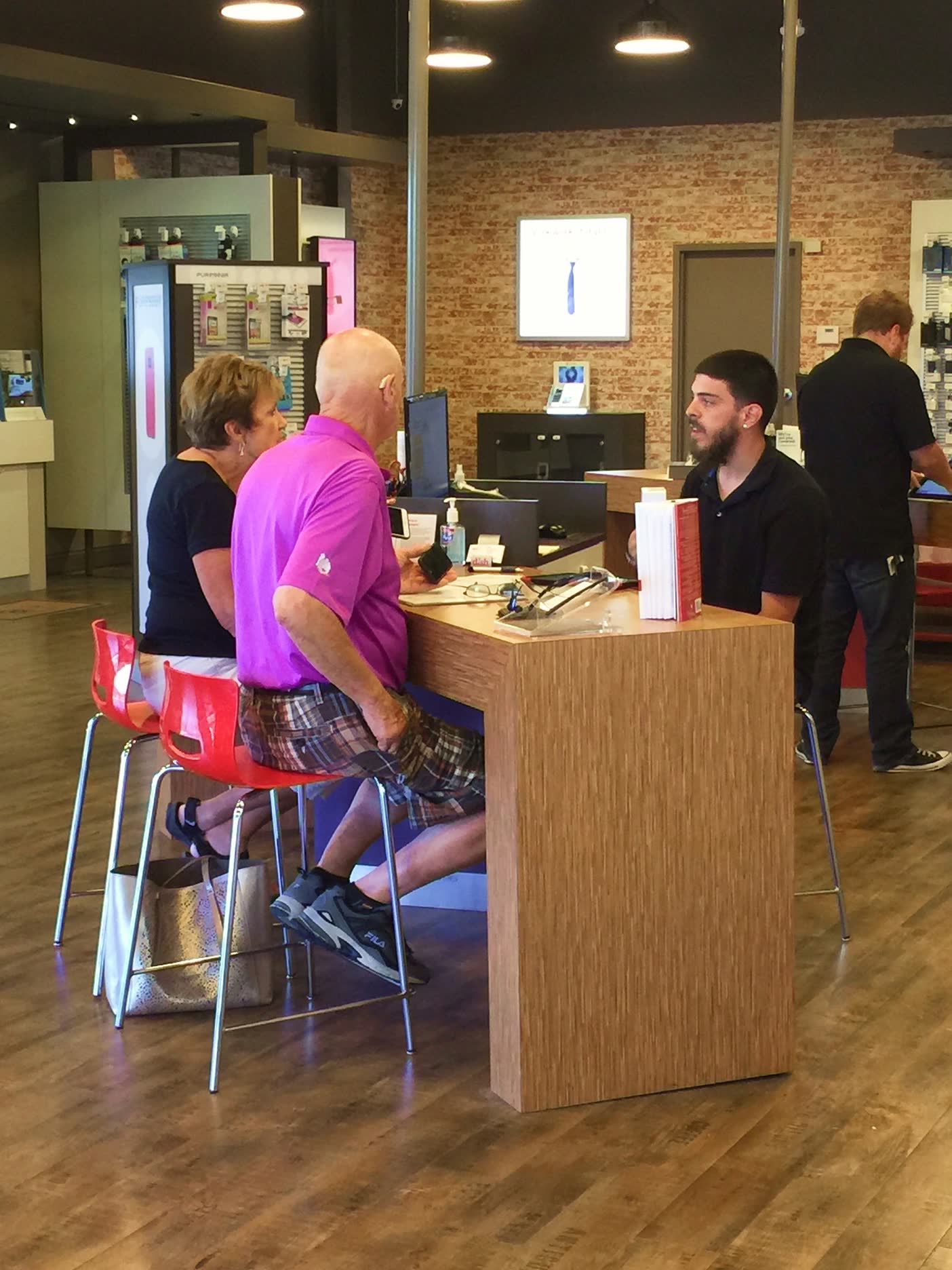 A sales consultant serving two customers across the counter of a TCC store