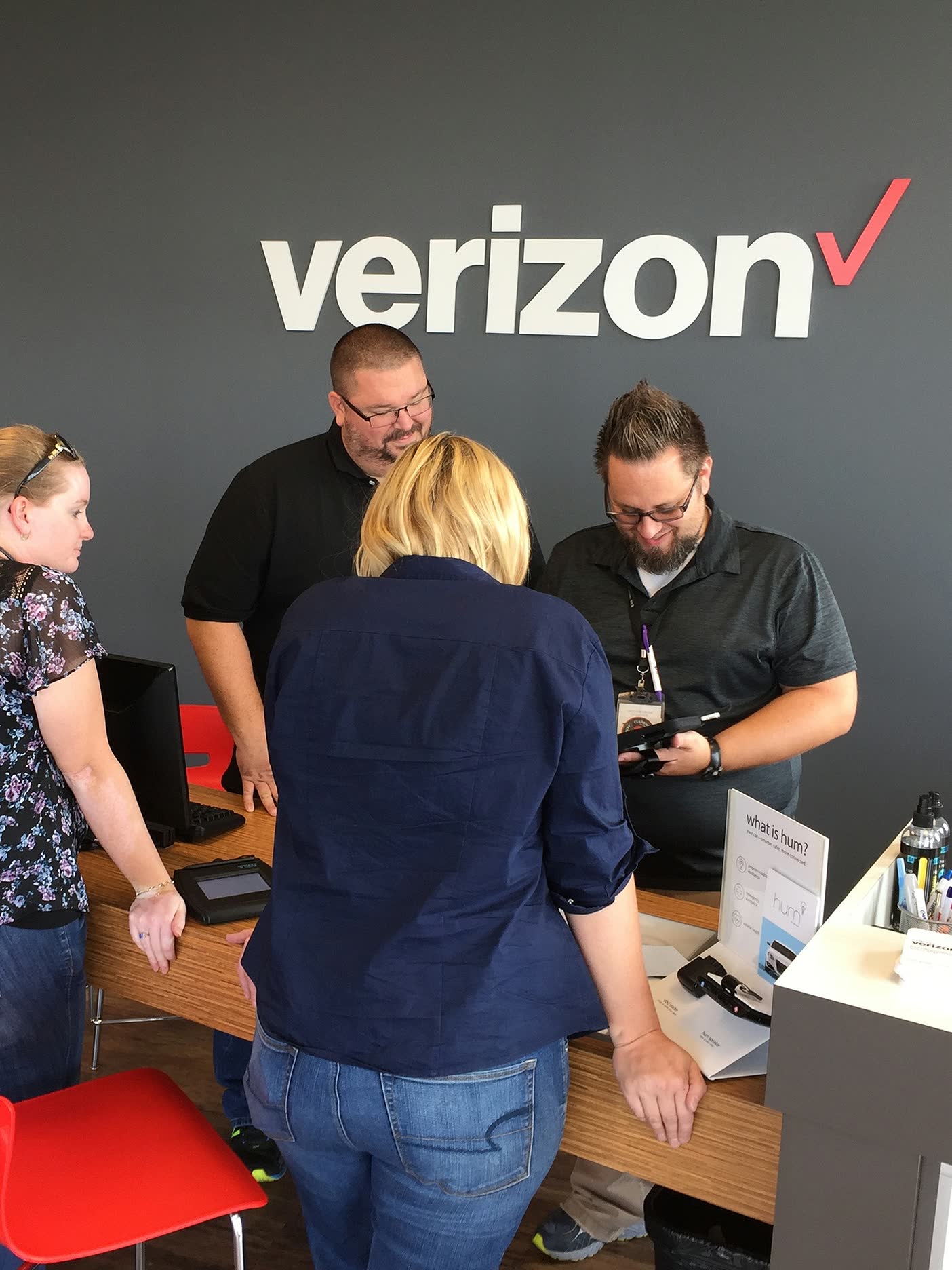 Store staff gathered around a tablet under the Verizon sign, trying the app